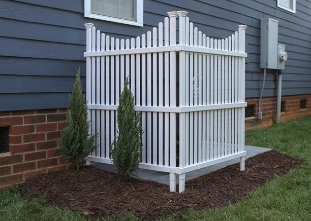a white picket fence screen hiding trash bins
