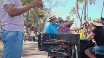 GIF of someone grilling in the foreground while people cheers in the background