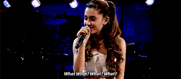 A GIF of Ariana Grande with a microphone in her hand saying &quot;What?&quot; numerous times