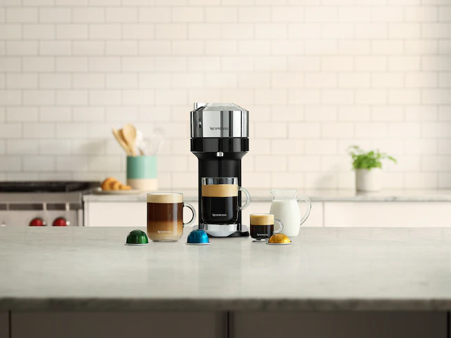 A Nespresso coffee maker on a counter with cups of coffee beside it