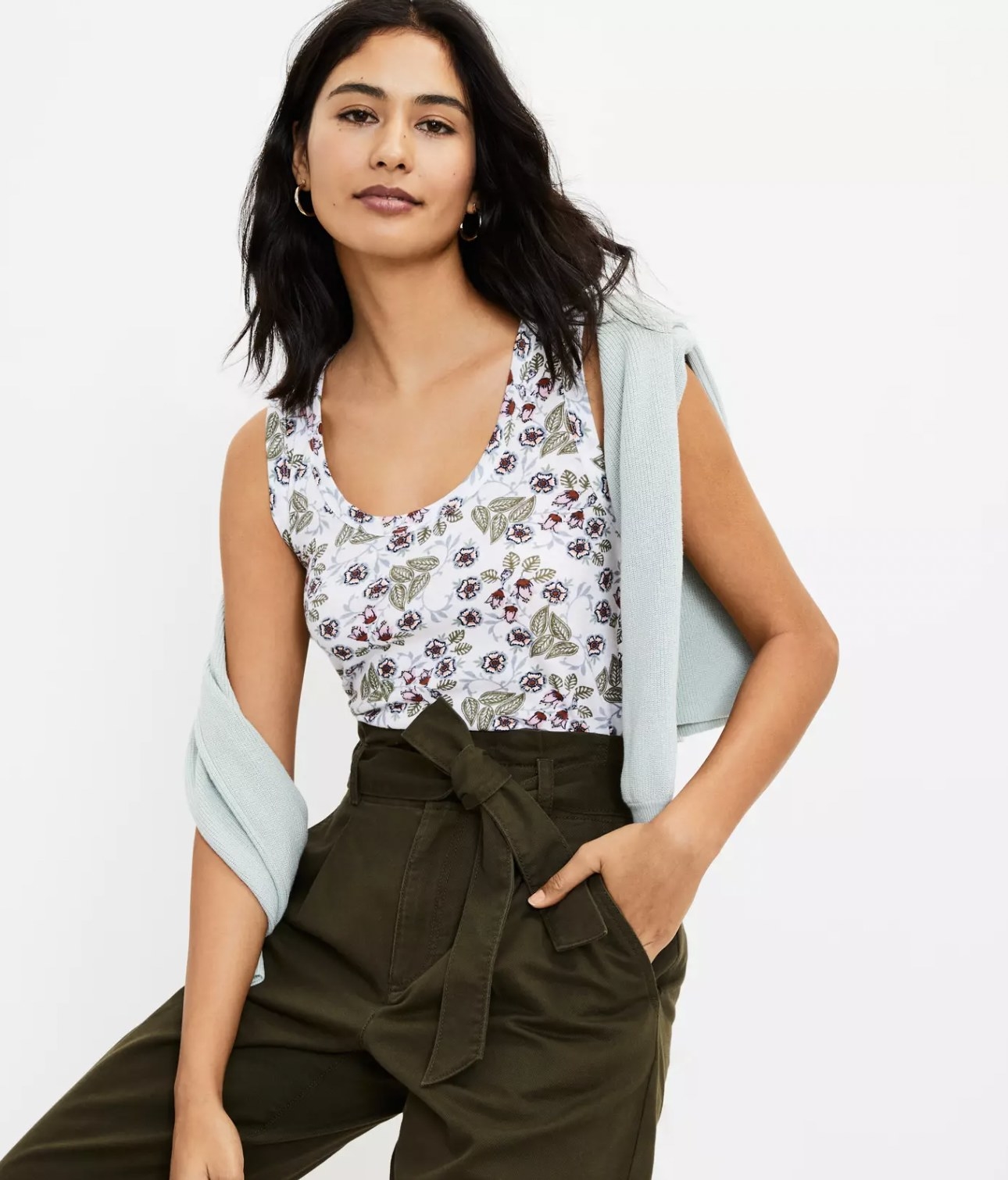 model wearing the floral tank tucked into green paperbag pants with sweater draped over shoulder