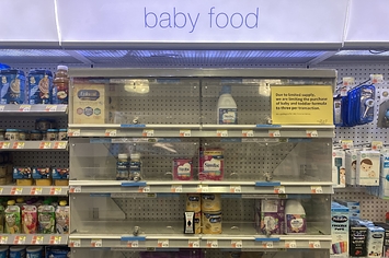 A security case in a pharmacy with a sign that reads "Due to limited supply, we are limiting the purchase of baby and toddler formula to three per transaction"