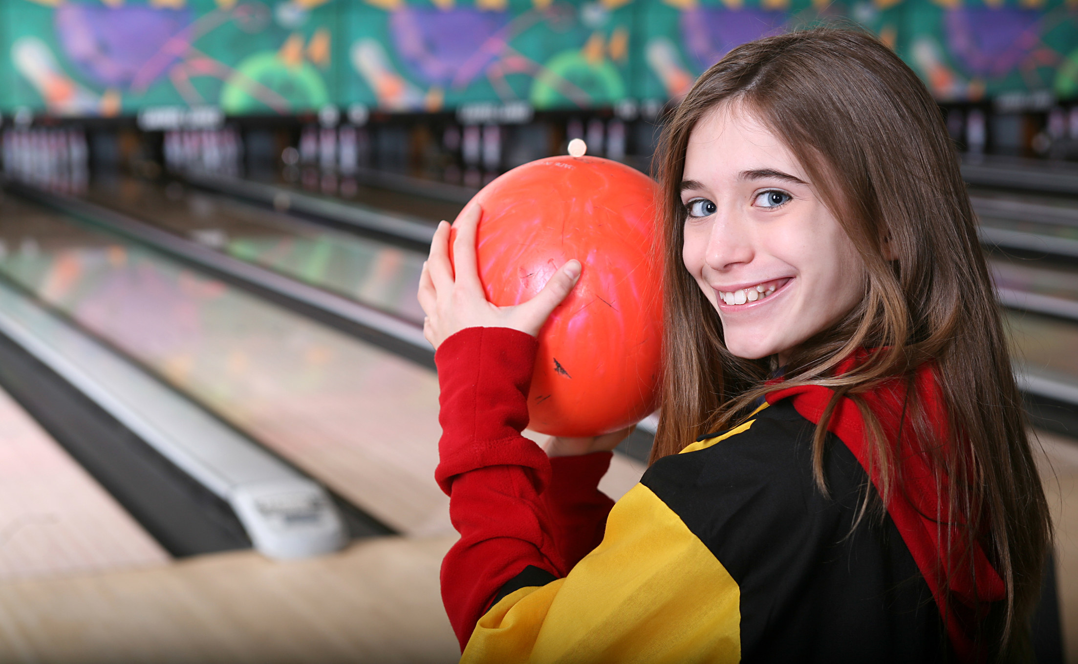 A girl at a bowling alley holding a bowling ball and smiling