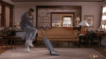 A man happily vacuuming the floor.