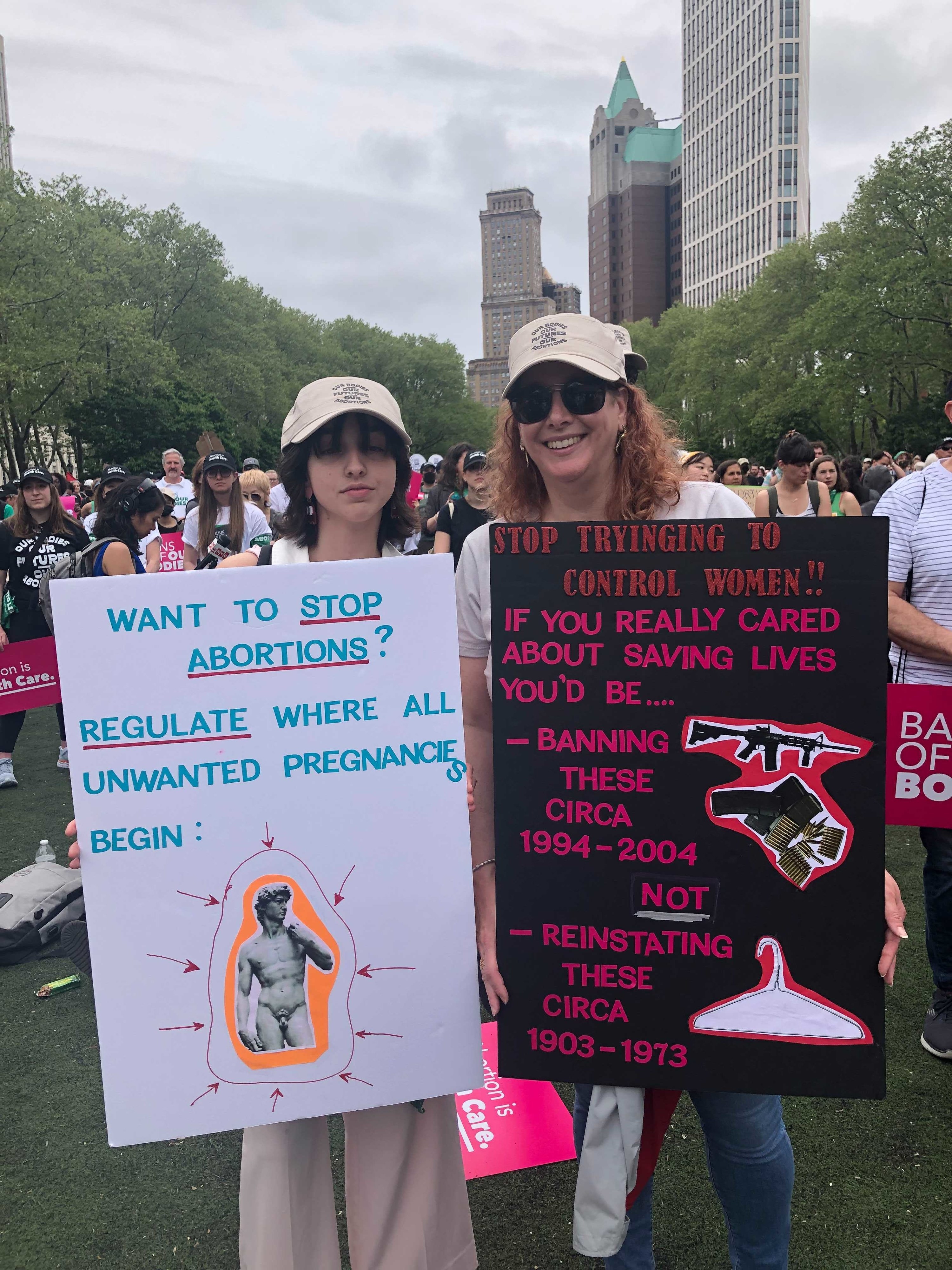 &quot;Want to stop abortions? Regulate where all wanted pregnancies begin:&quot; with sign pointing to a penis, and &quot;If you really cared about saving lives you&#x27;d be banning these [guns] circa 1994–2004, not reinstating these [hangers] circa 1903–1973&quot;