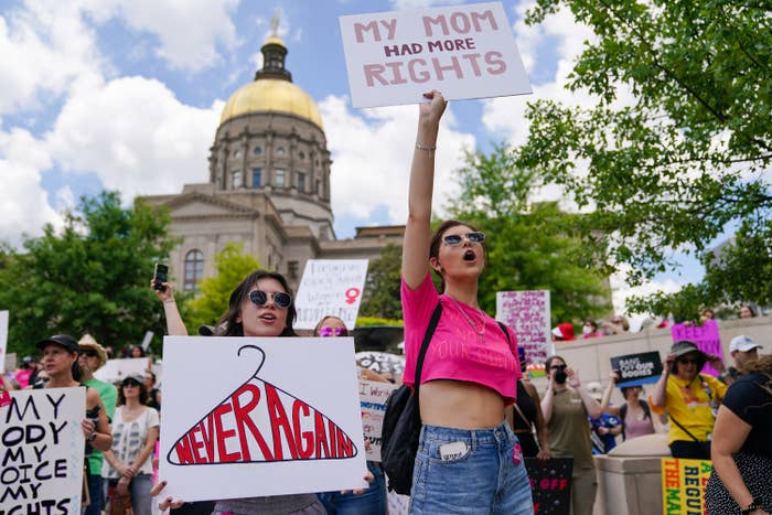 A group of protestors, including one holding a sign with &quot;Never Again&quot; inside a coat hanger