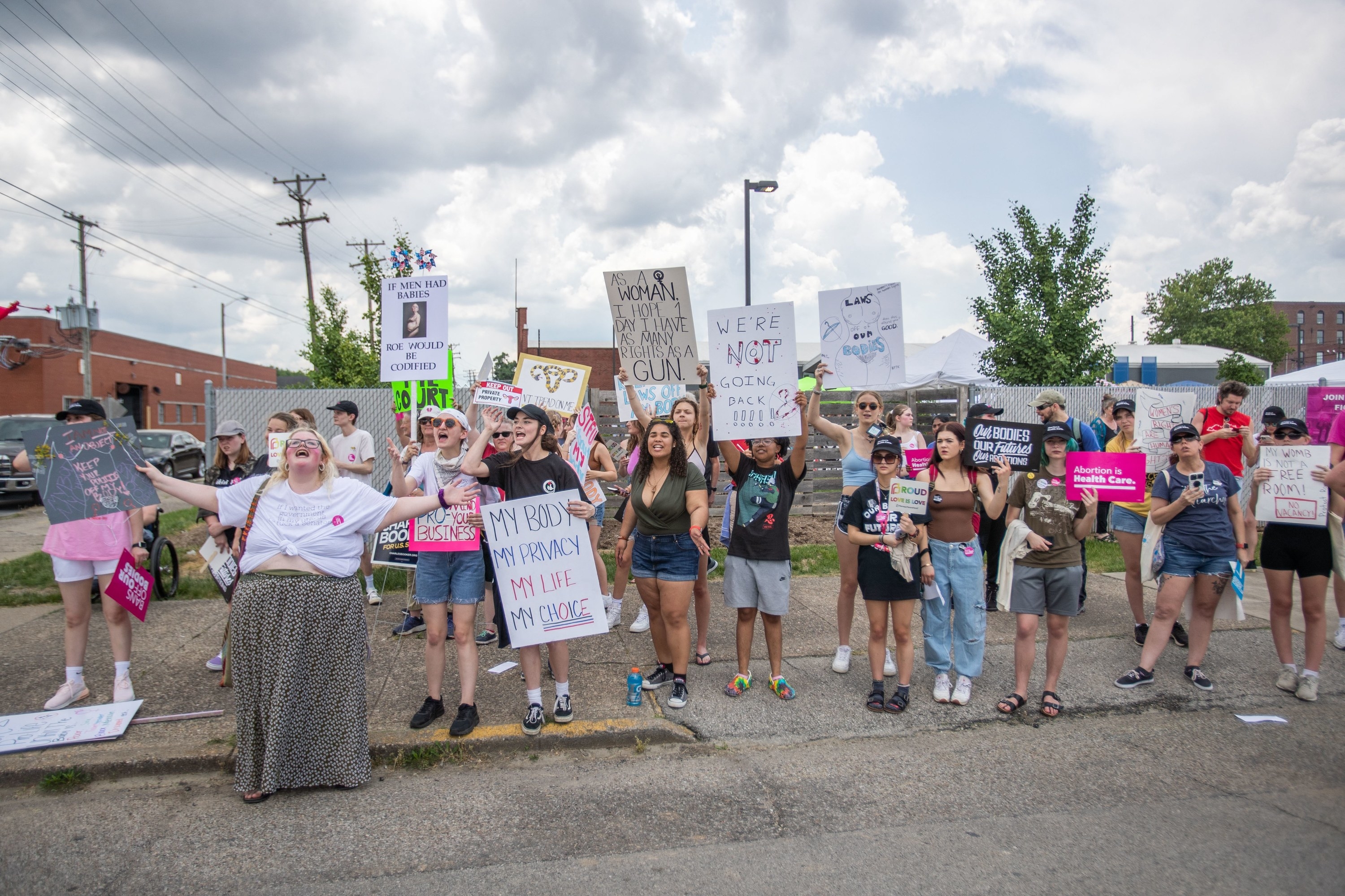 People on the sidewalk hold up signs, including &quot;My body, my privacy, my life, my choice&quot;