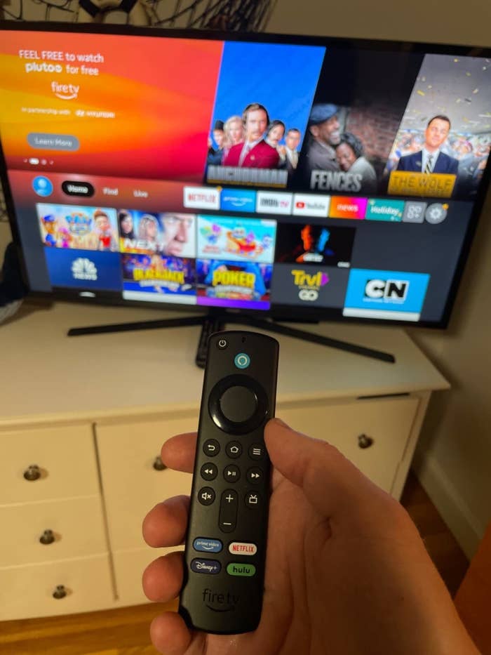 reviewer holding the fire stick remote pointed at home page on tv