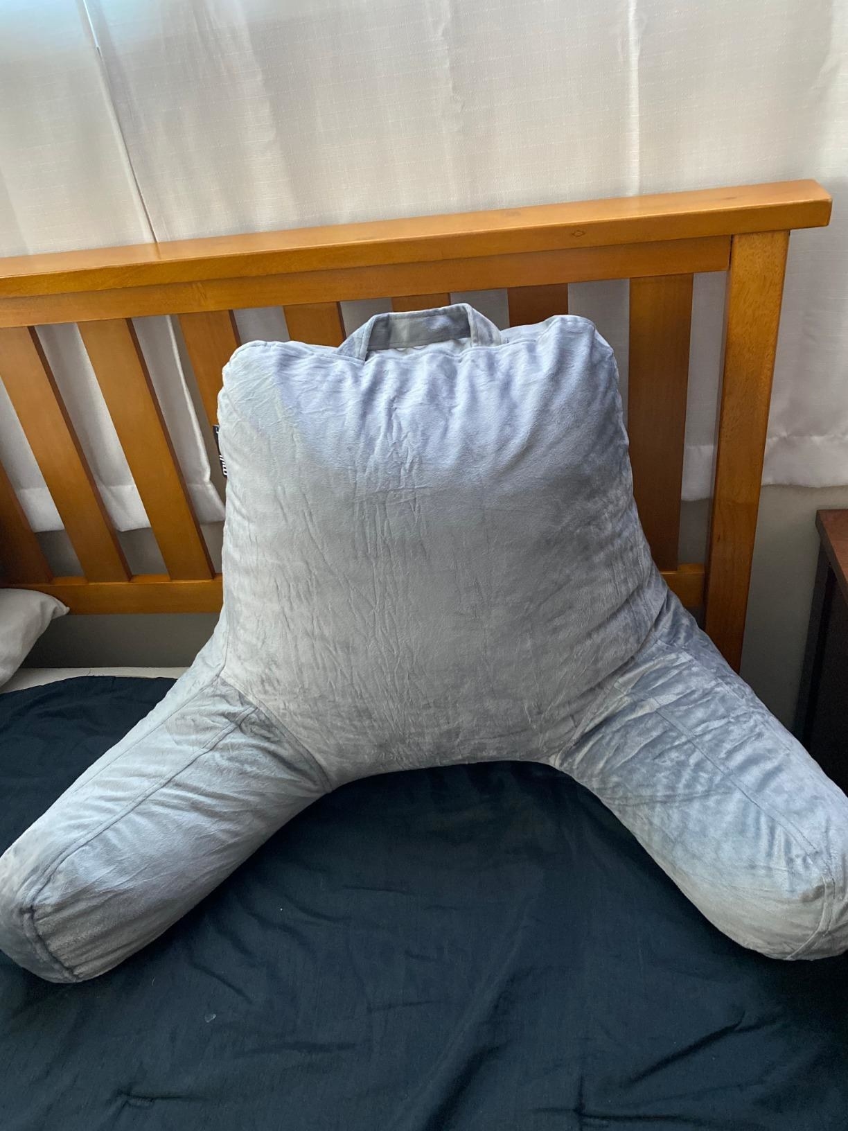 reviewer&#x27;s photo of the grey shiny pillow resting against headboard on bed