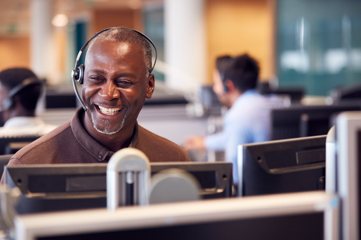 A man with a headset behind a computer laughing