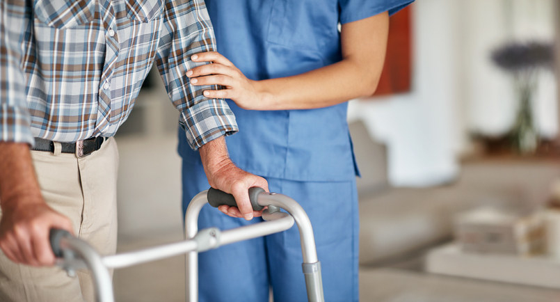 A nurse helping an older gentleman use a walker