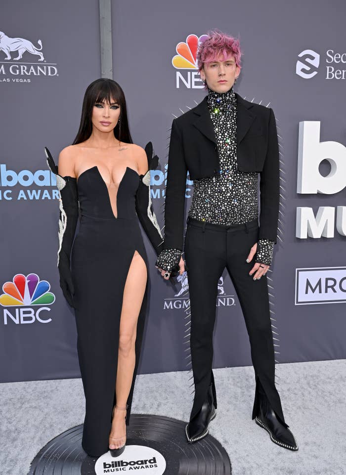 Megan, in a thigh-high slit gown, holds hands with MGK at the BBMAs red carpet