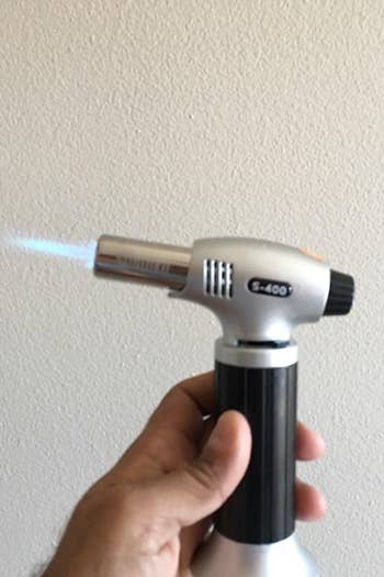a reviewer holding the blow torch with a blue flame coming out of it