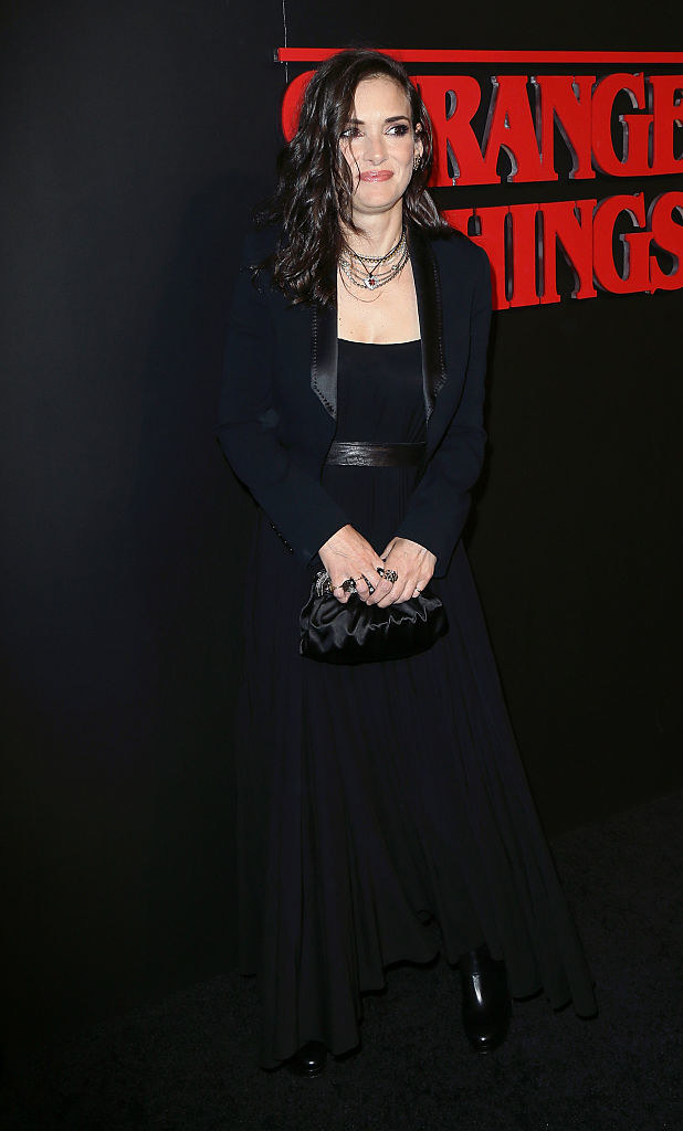 Winona decked out in all black with a dress, jacket, shoes, and handbag