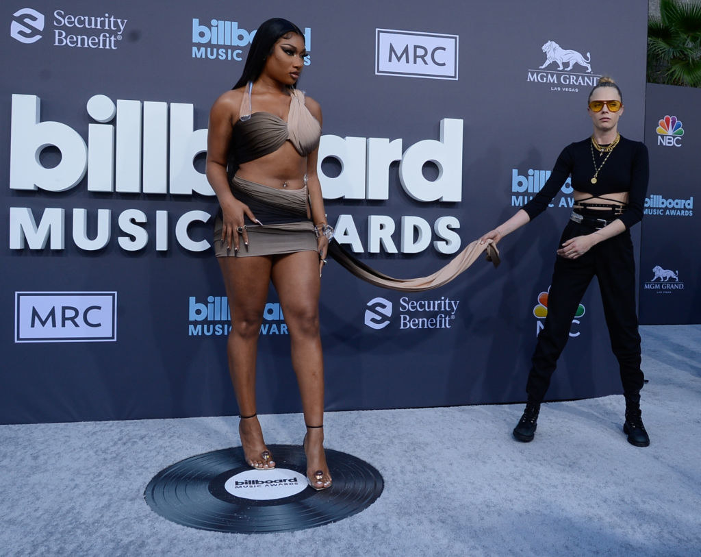 Megan The Stallion posing while Cara Delevingne awkwardly holds an extended piece of Megan&#x27;s dress