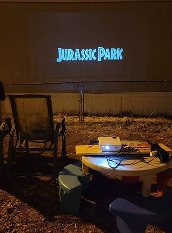 reviewer photo of the projector showing jurassic park against the side of a house