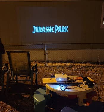 reviewer photo of the projector showing jurassic park against the side of a house