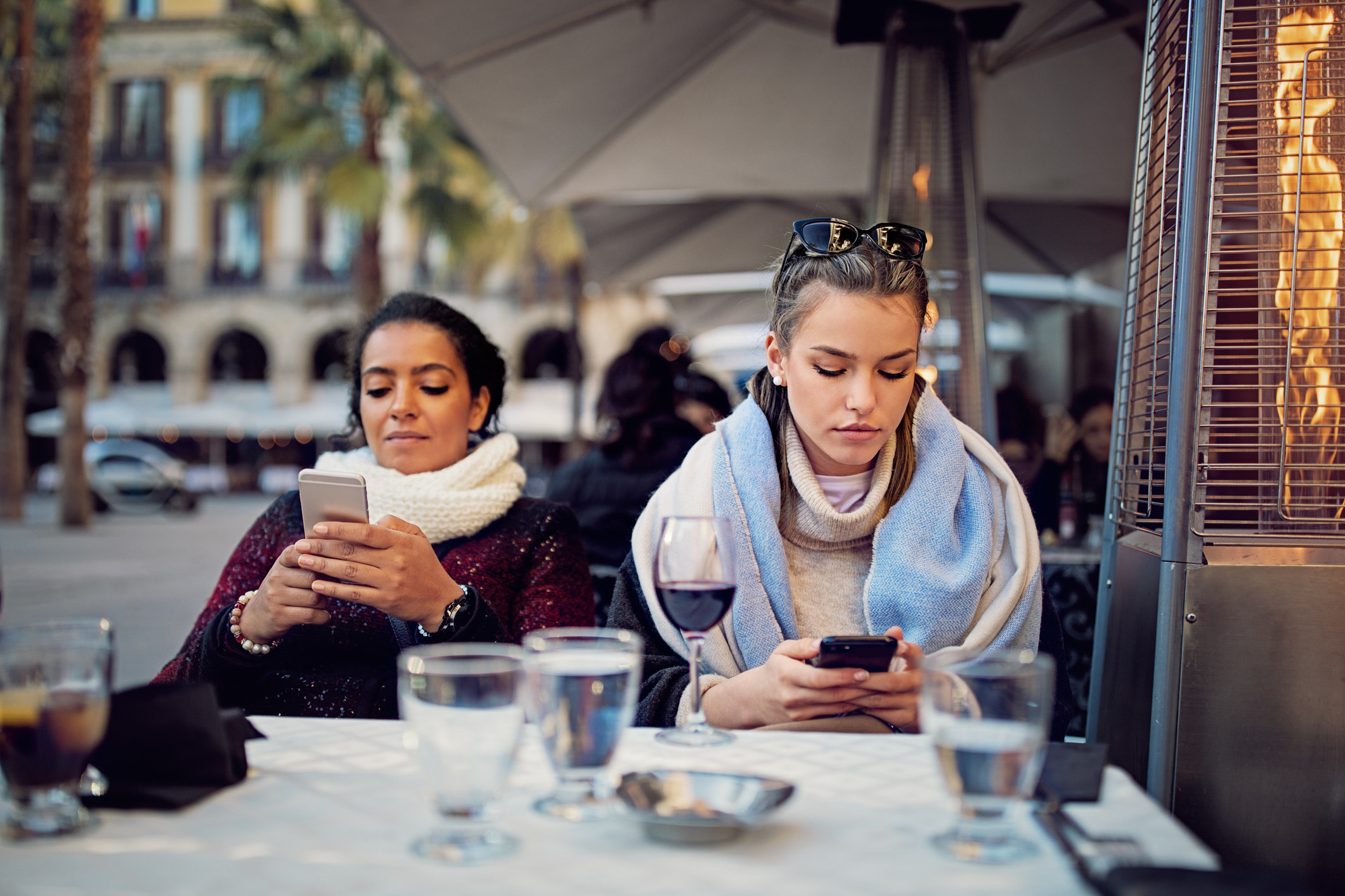 Two women at table texting separately on their phones