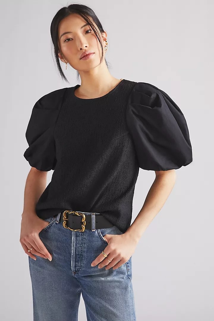 A model wearing the blouse, tucked into jeans, in the color Black