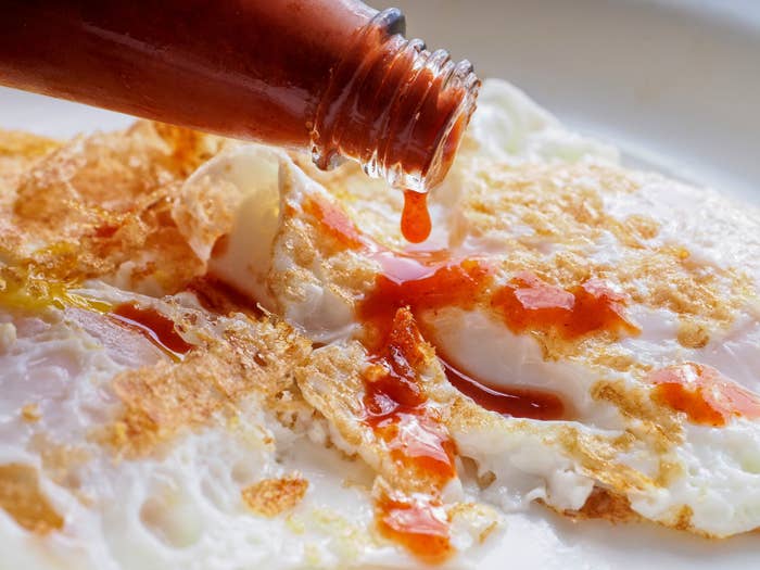 Pouring hot sauce on fried eggs