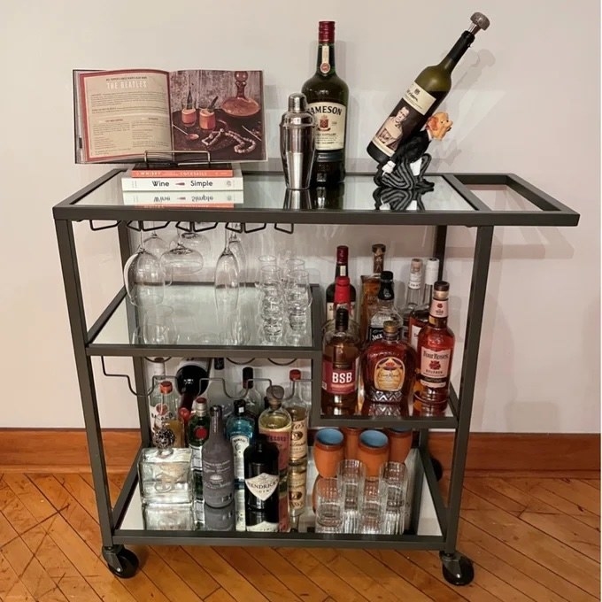 A gray bar cart with glasses and drinks on it