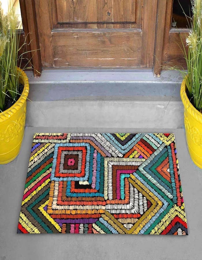 the colorful doormat in front of a door between two plants