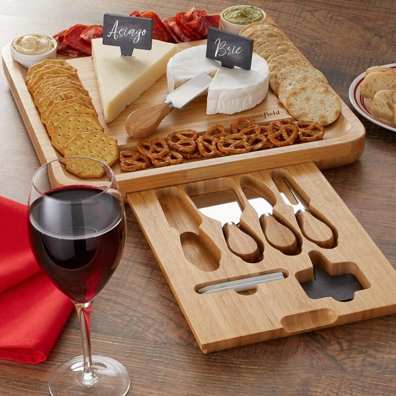 the cheeseboard with cheese and other food on it with a glass of red wine