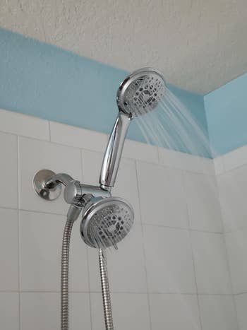 Dual shower heads attached to a bathroom wall, with water flowing from one of them