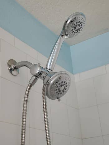 Dual shower heads attached to a wall, one fixed and one handheld, in a tiled shower area