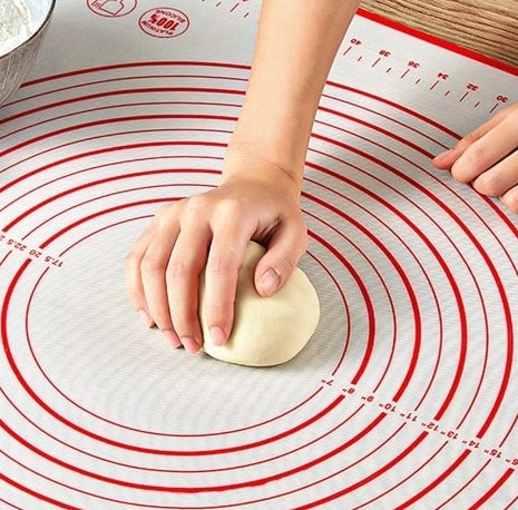 The baking mat with a ball of dough on it that a person is rolling
