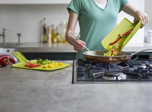 Model is pouring vegetables they chopped on the board into a frying pan
