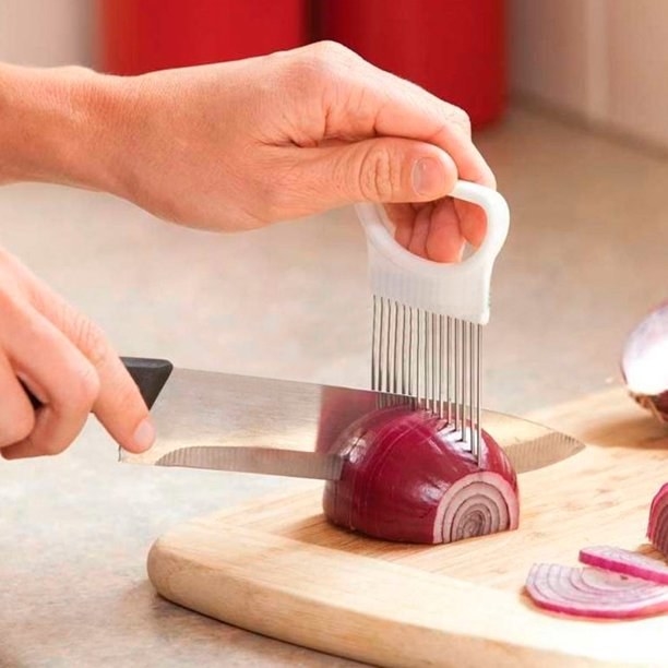 A person is holding the slicer guide on an onion and using a knife to slice it