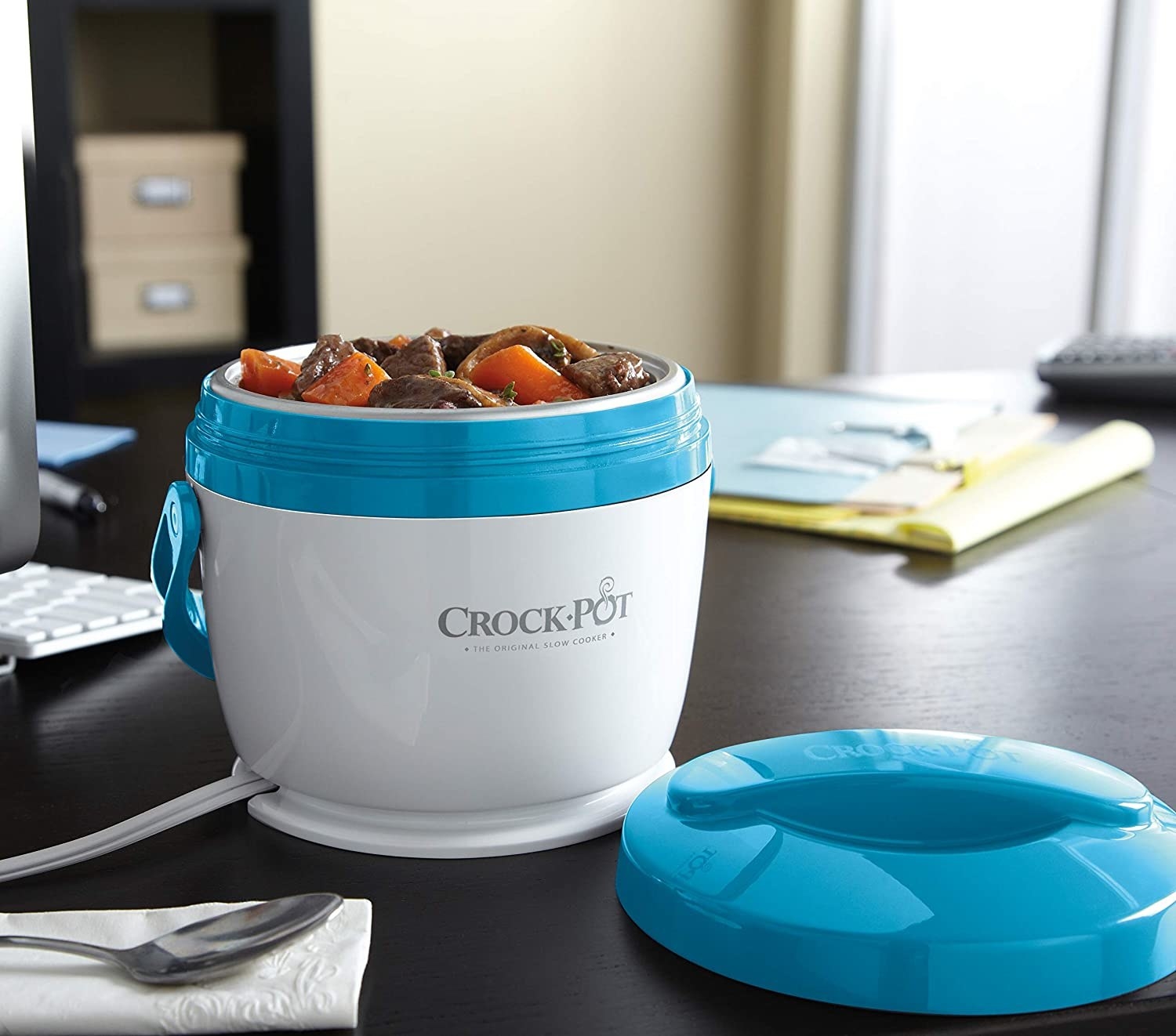 The Crock-Pot on a desk with beef stew in it and the lid beside it