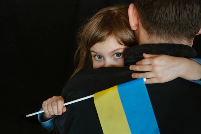 A man holding his little girl, as she holds a Ukrainian flag