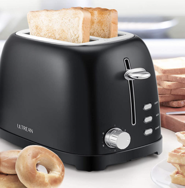 The toaster with two slices of toast in it, next to piles of bagels, bread, and a plate of waffles