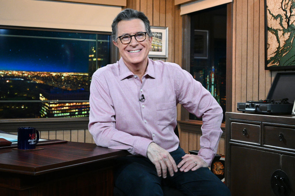 Stephen Colbert smiles at a desk