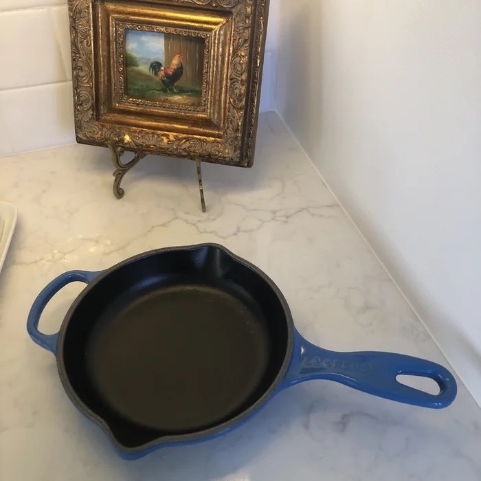 A small blue cast iron skillet in a reviewer&#x27;s kitchen with a chicken painting