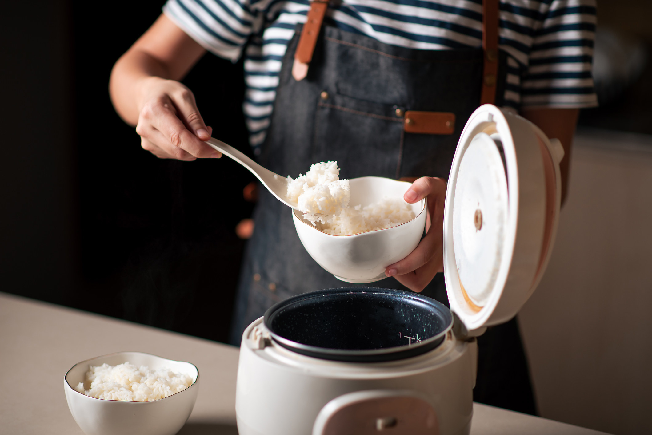 A person putting rice from a rice cooker into a bowl