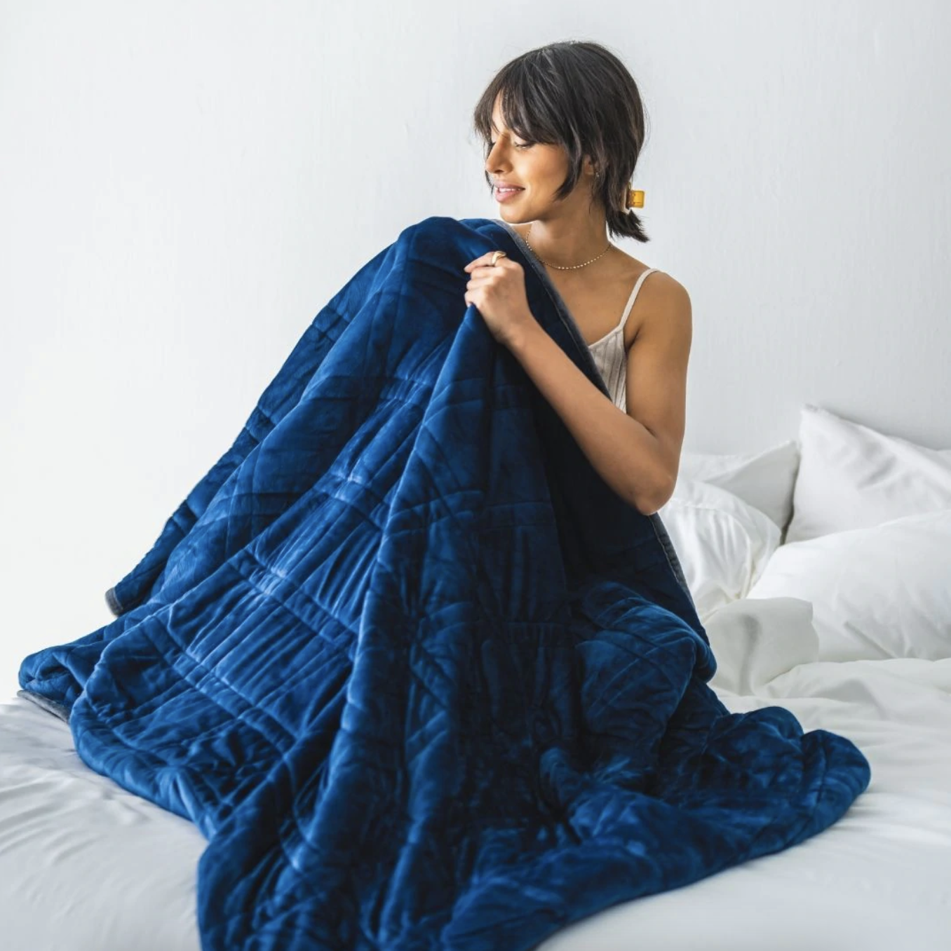 model sitting on a bed wrapped in the blue weighted blanket