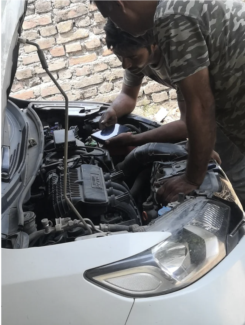 two people watching a video on a phone while they fix a car