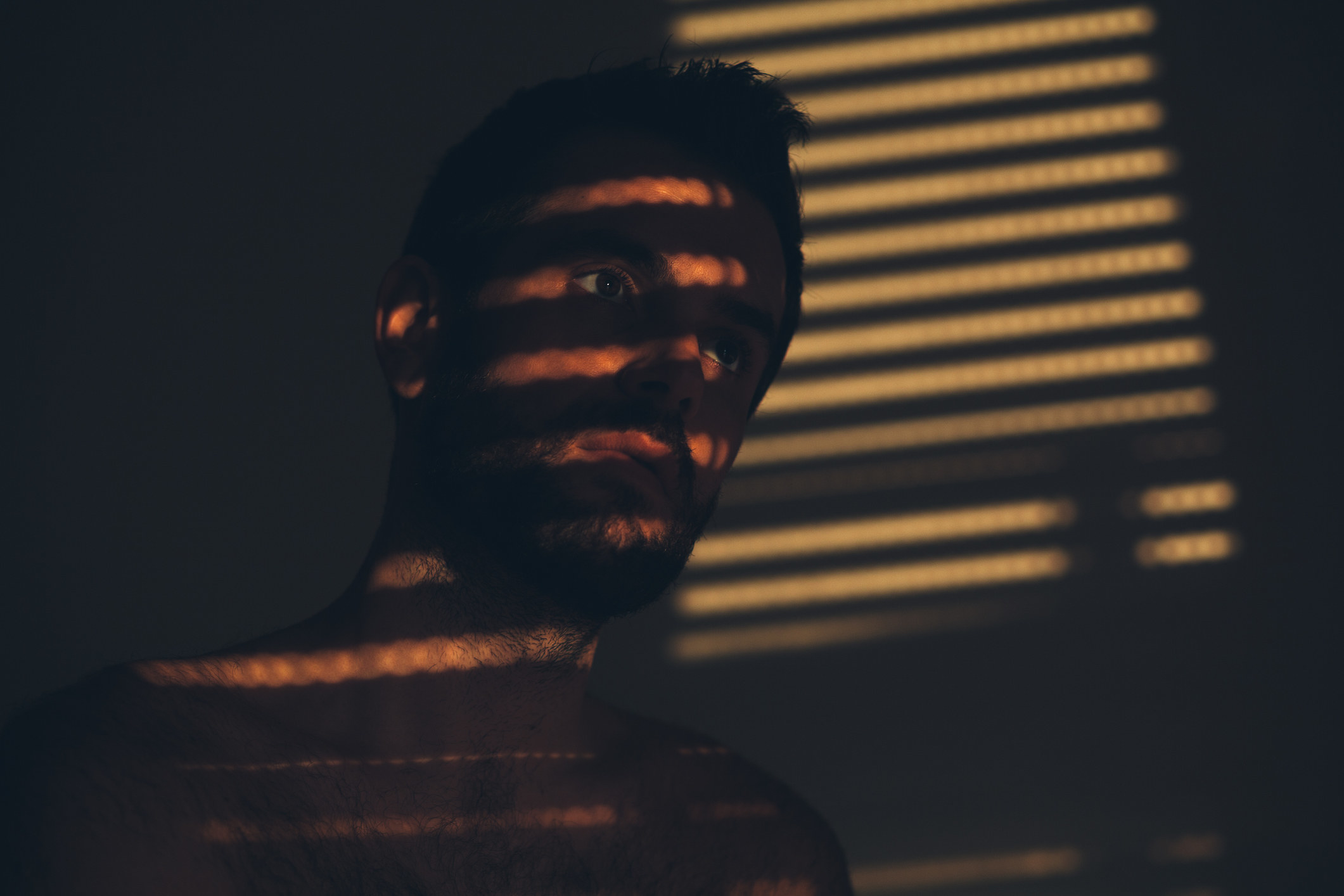 a person in a dark room with light coming in from the blinds