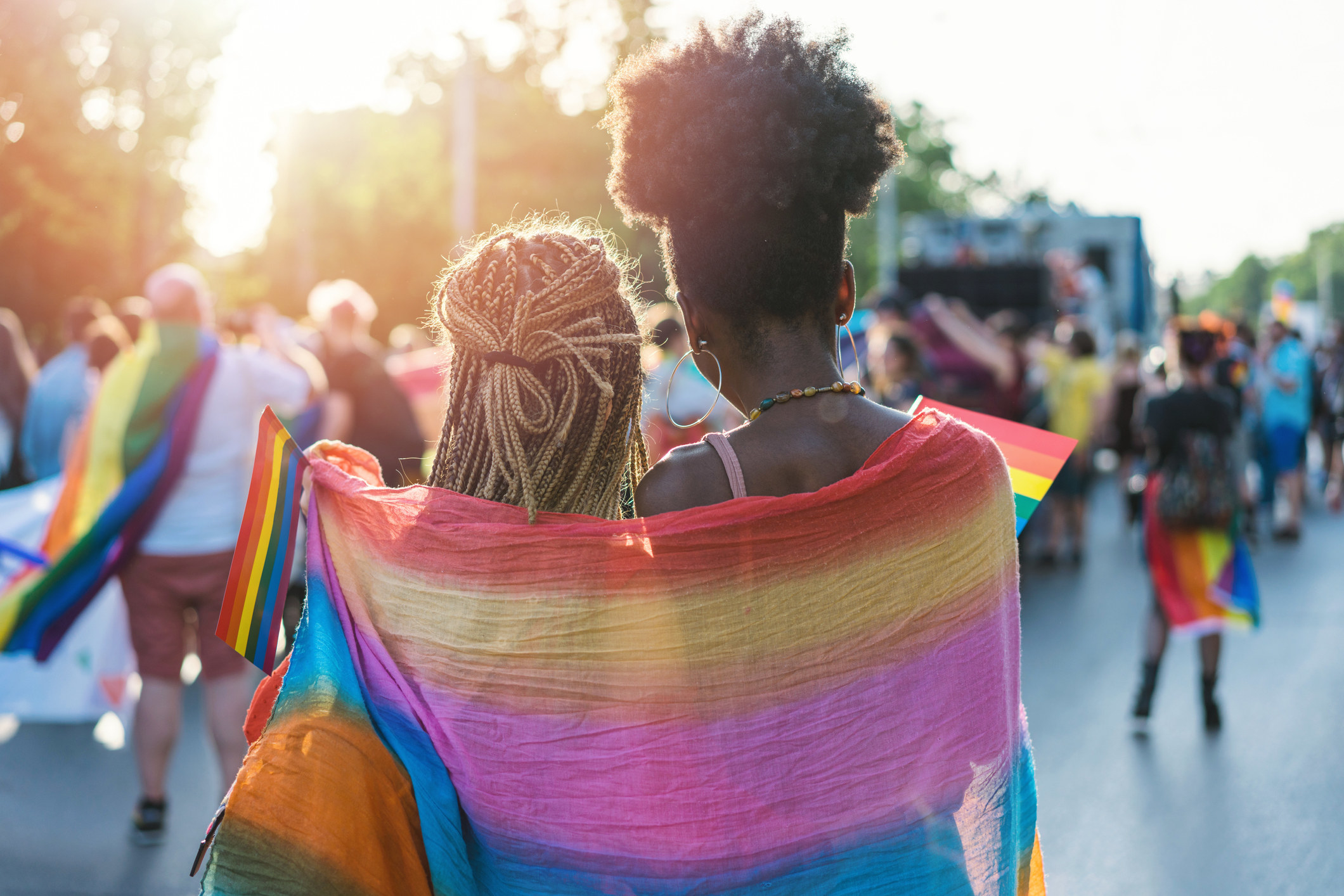 two women wrapped in a rainbow shawl watching the gay pride parade