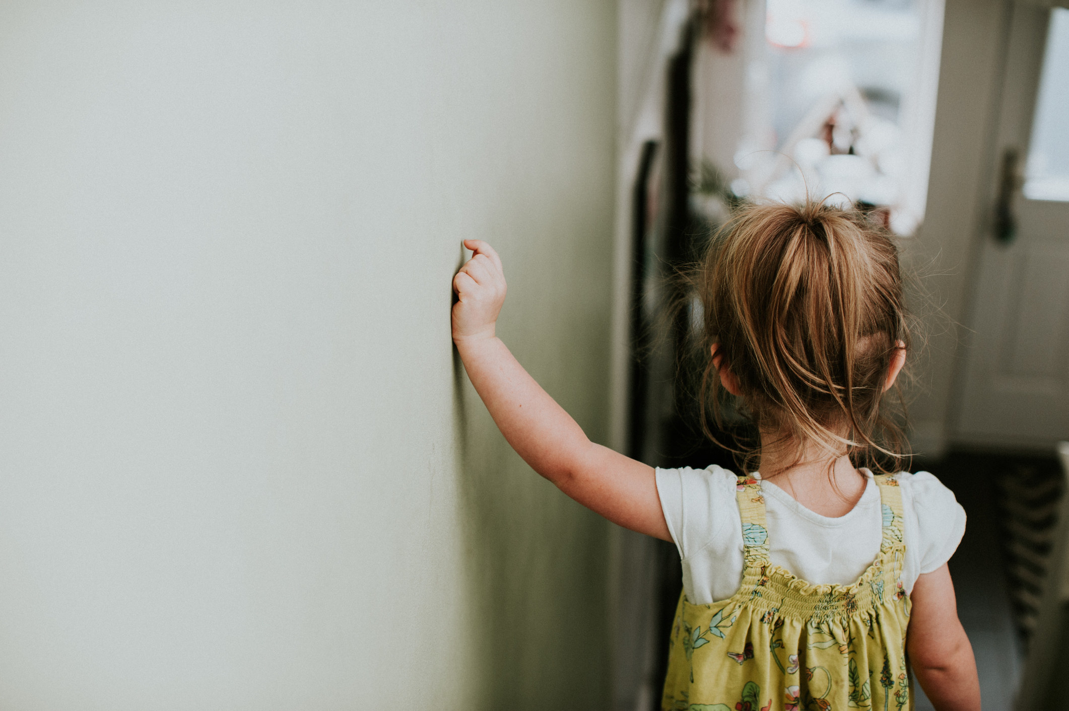 a toddler walking with their hand on the wall