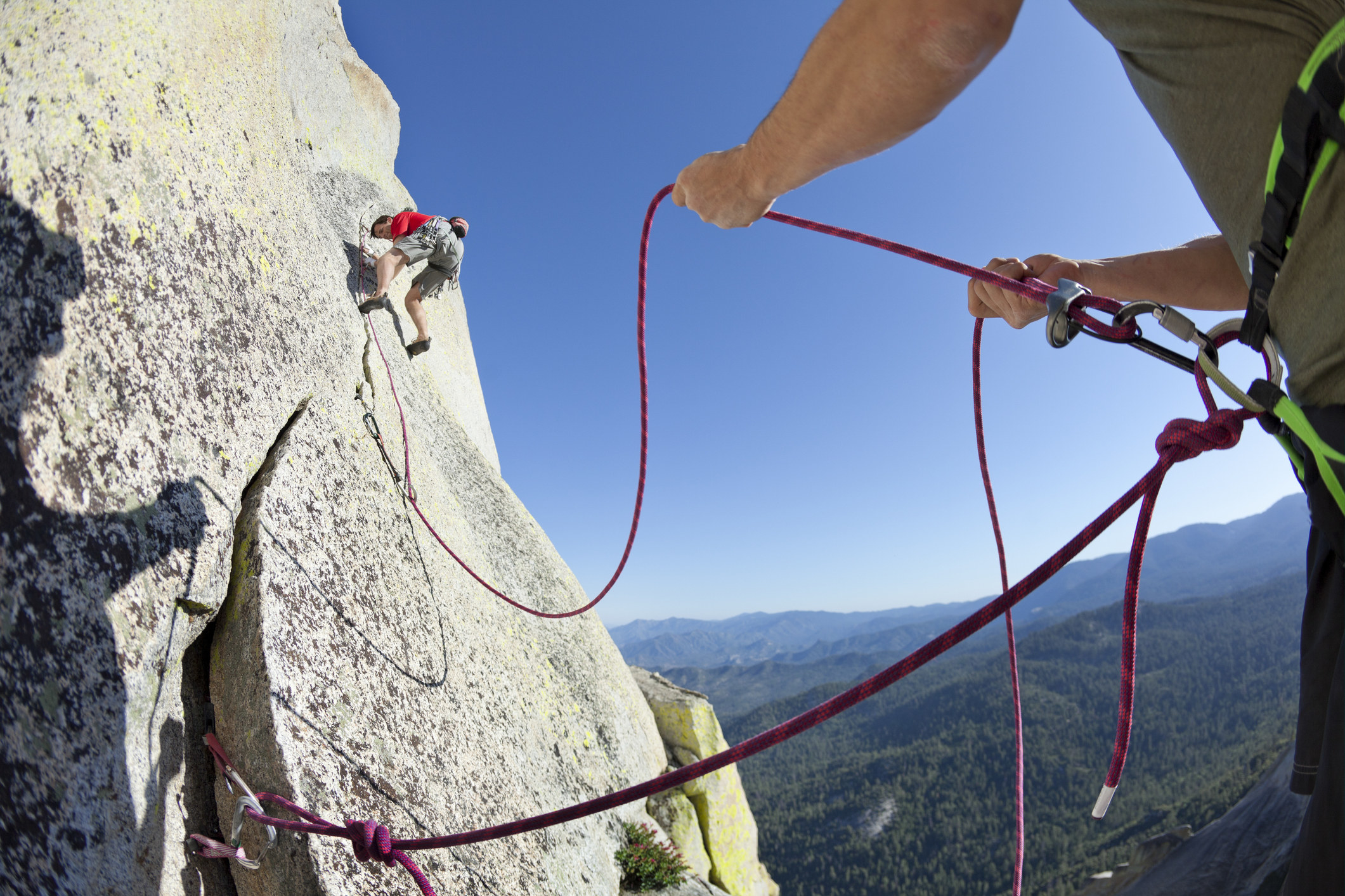 someone holding ropes on the ground while some rock climbs