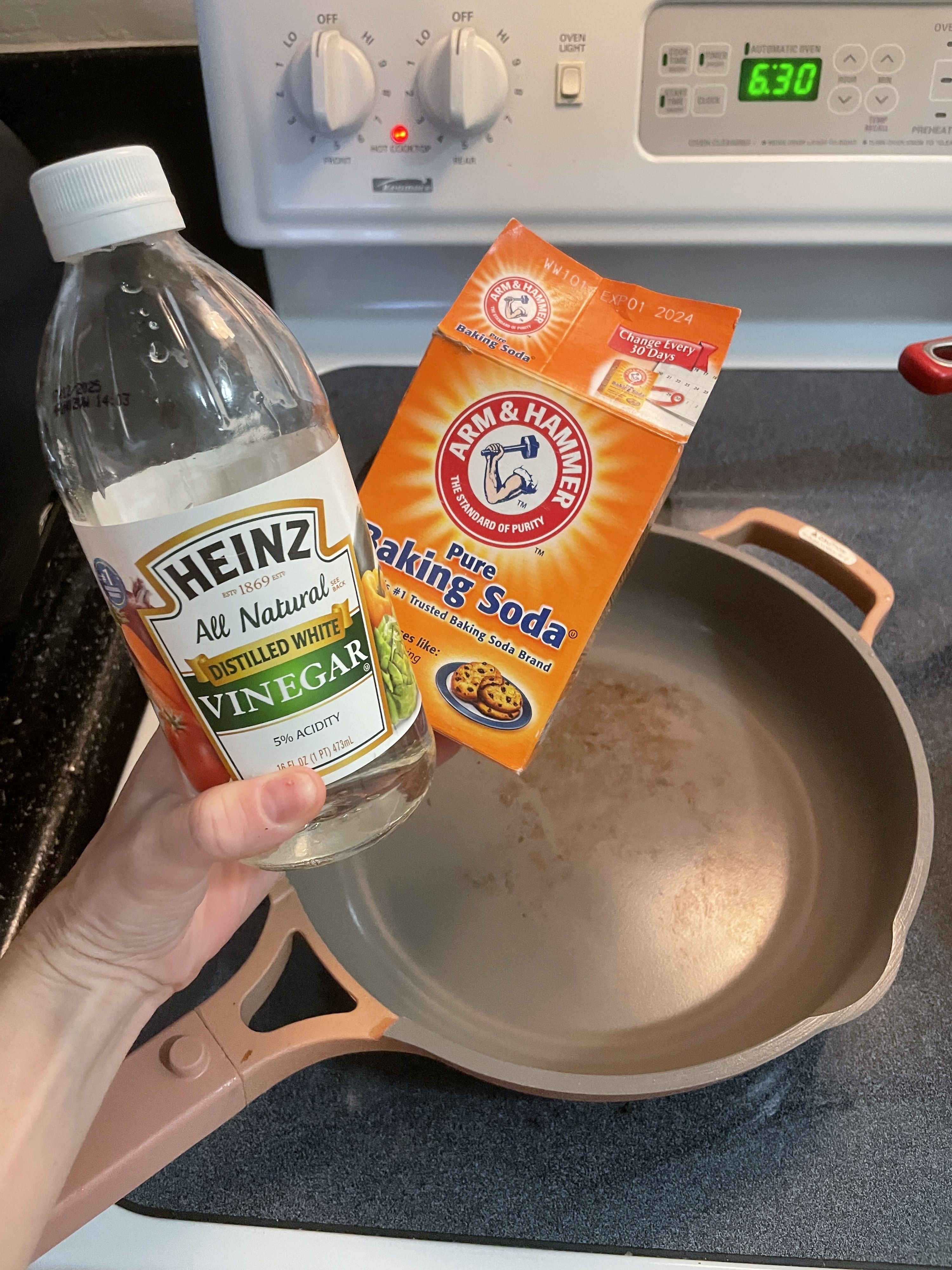 A bottle of white vinegar and a box of baking soda held above the pan on the stove top