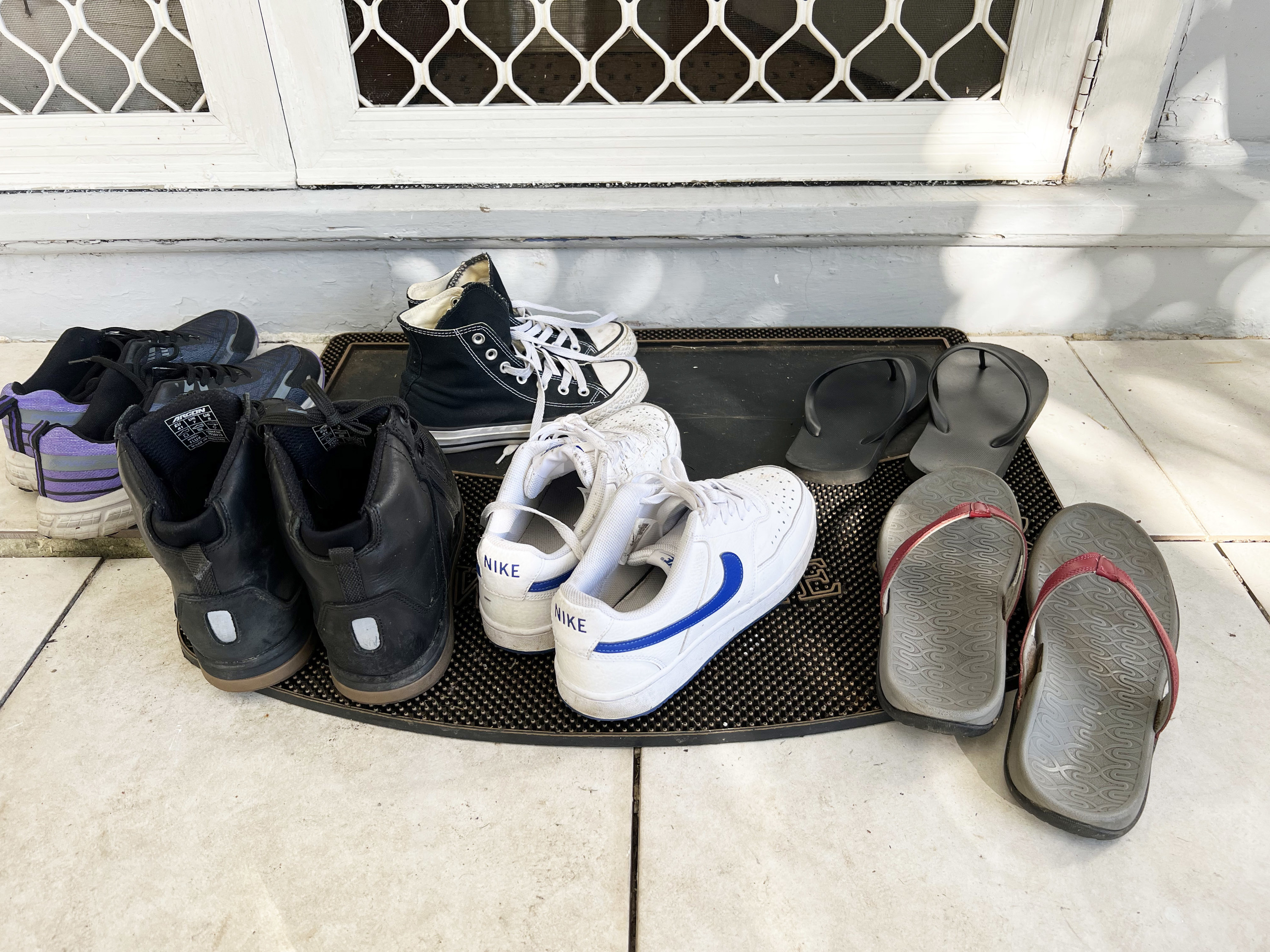 Various pairs of shoes placed on a welcome mat by the door
