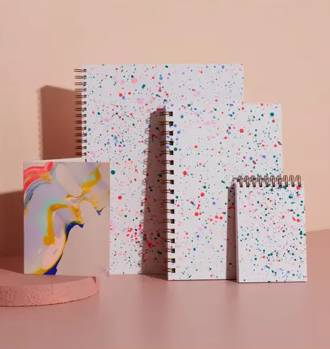Three notebooks of different sizes leaning against a wall