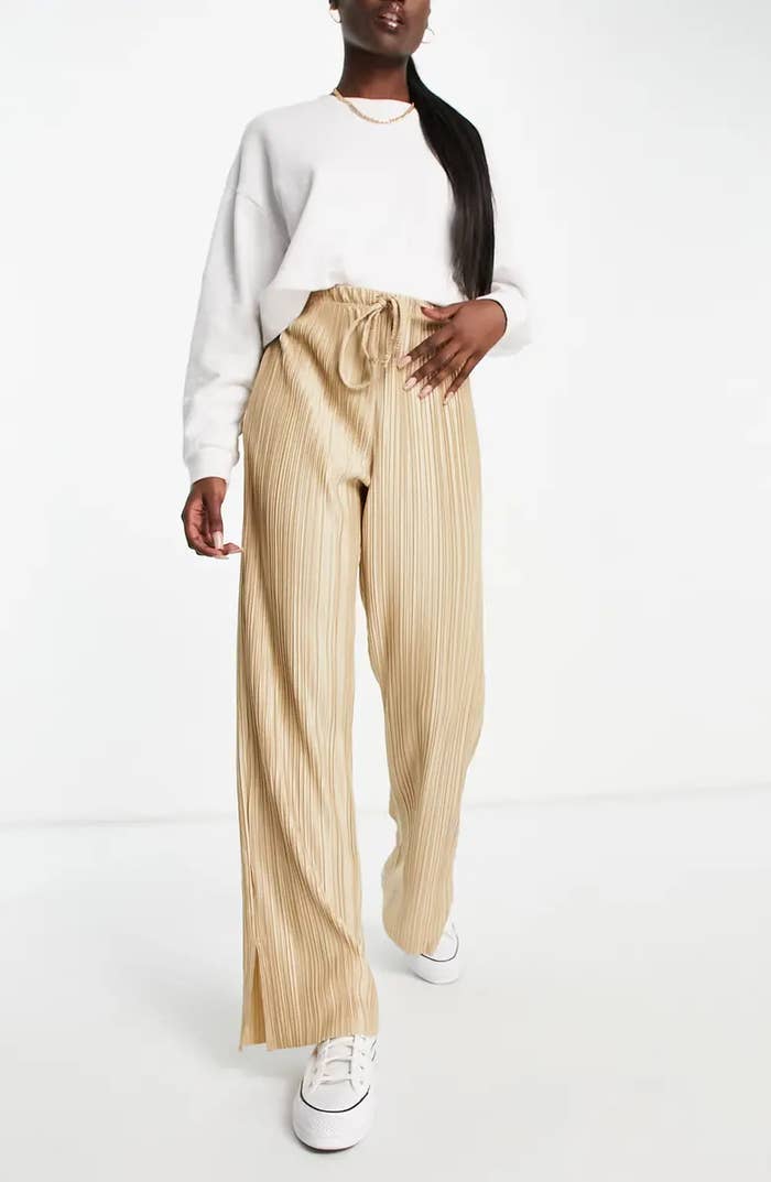 A person wearing tan plisse pants with a white long sleeved shirt