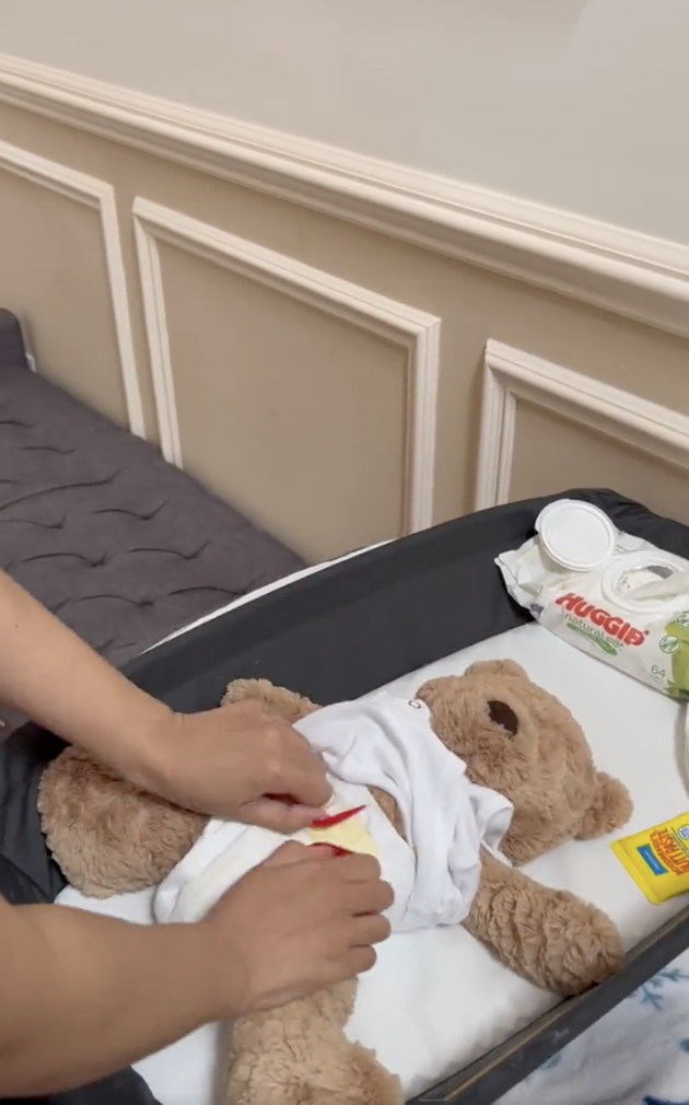 close up of Cardi&#x27;s hands putting on a diaper on a teddy bear