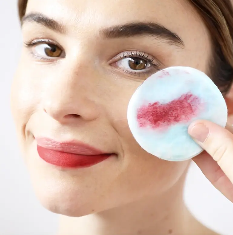 A person holding up a cotton round that has lipstick on it